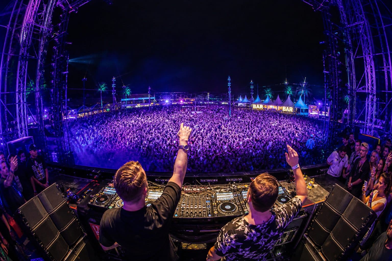 Festival ao ar livre com DJ e plateia iluminada em azul e roxo